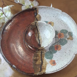 May include: A ceramic serving dish with a divided section for dips and a larger section for snacks. The dish is decorated with a floral pattern and has a speckled glaze.