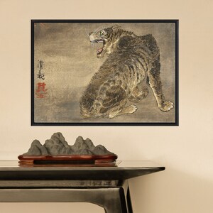 K&ouml;nnte beinhalten: Ein gerahmtes Gem&auml;lde eines knurrenden Tigers mit gr&uuml;nen Augen vor beigefarbenem Hintergrund. Der Tiger ist in sitzender Position dargestellt, mit dem Schwanz um seinen K&ouml;rper gewickelt. Das Gem&auml;lde ist in japanischen Schriftzeichen in der oberen linken Ecke signiert.