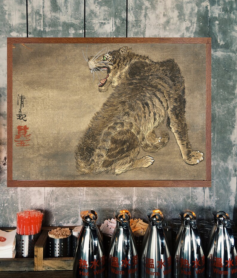 K&ouml;nnte beinhalten: Ein gerahmtes Gem&auml;lde eines braunen und wei&szlig;en Tigers mit gr&uuml;nen Augen, der mit offenem Maul br&uuml;llt. Das Gem&auml;lde ist auf einem beigefarbenen Hintergrund mit roten japanischen Schriftzeichen. Das Gem&auml;lde h&auml;ngt an einer grauen Wand.