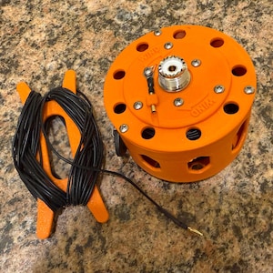 May include: An orange electronic device with multiple circular openings and silver hardware. A black cable is connected to the device, and a separate orange holder contains a coiled black cable. The word "WIND" is printed on the device.