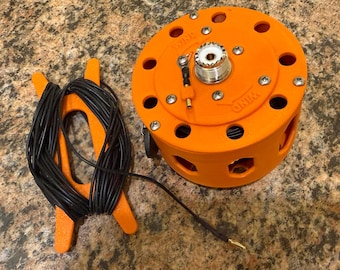 May include: An orange electronic device with multiple circular openings and silver hardware. A black cable is connected to the device, and a separate orange holder contains a coiled black cable. The word "WIND" is printed on the device.