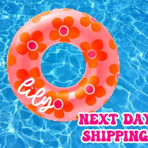 May include: A pink inflatable pool float with an orange floral pattern. The float has a hole in the center for a person to sit in. The text "lily" is written on the float.