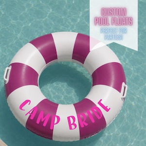May include: A white and magenta striped pool float with the words "Camp Bride" in magenta. The float is in a pool of water. The text "Custom Pool Floats Perfect For Parties!" is in the upper right corner.