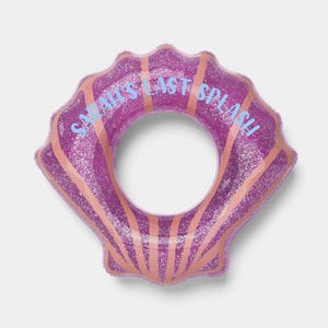 May include: A purple glittery inflatable pool float shaped like a seashell with light pink radial stripes. The text SARAH'S LAST SPLASH is printed in light blue across the top section of the float, which features a central circular opening.