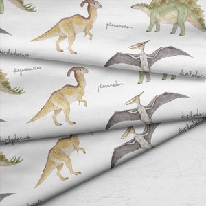May include: White fabric with a repeating pattern of watercolor dinosaurs. The design includes various dinosaurs such as the Parasaurolophus, Stegosaurus, and Pteranodon, with their names written in cursive.