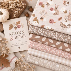 Pode incluir: Uma pilha de seis tecidos dobrados em tons neutros com padrões de coelhos, pássaros, abóboras, bolotas, rosas, folhas e xadrez vichy. Um cartão com a etiqueta ACORN & ROSE A FABRIC COLLECTION BY PRINTING FABRICS está ao lado.