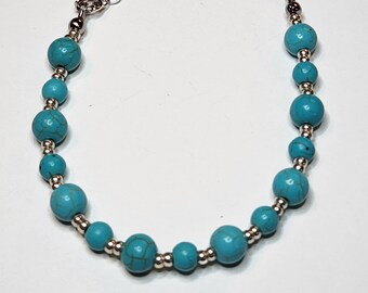 Puede incluir: Un brazalete de cuentas turquesa con una cadena y un cierre plateados.
