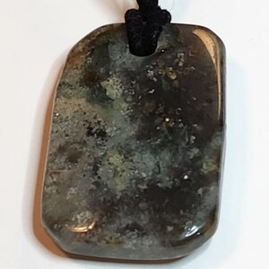 May include: A dark green and black stone pendant with a speckled pattern, hanging from a black cord.