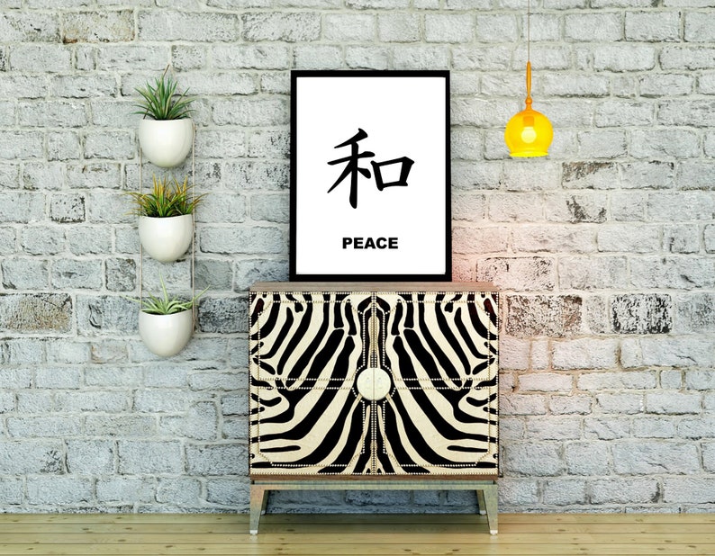 May include: A black and white zebra print cabinet with a black frame and gold accents. A black framed print with the Japanese character for peace and the word "peace" underneath is hanging on a white brick wall above the cabinet. There are three white hanging planters with green plants on the wall to the left of the cabinet. A yellow globe pendant light hangs from the ceiling above the cabinet.