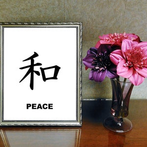 May include: A framed print with the Japanese character for peace, "和", and the word "PEACE" written below it. The print is displayed on a wooden table with a vase of pink and purple flowers.