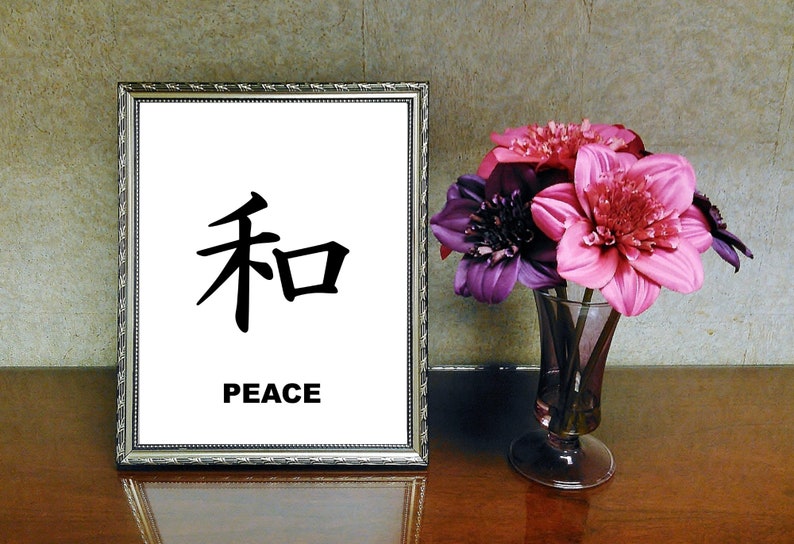 May include: A framed print with the Japanese character for peace, "和", and the word "PEACE" written below it. The print is displayed on a wooden table with a vase of pink and purple flowers.