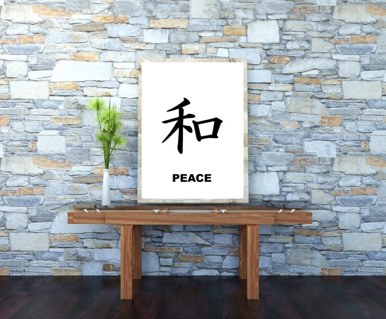May include: A white framed print with the Japanese character for peace, "和", and the word "PEACE" written below it. The print is hanging on a stone wall above a wooden table.
