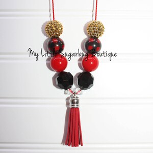 May include: Red, black, and gold beaded necklace with a red tassel. The beads are a mix of plaid, solid, and sparkly.