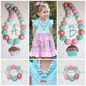 May include: A set of three necklaces featuring large, colorful beads and cupcake charms. The necklaces are made of pink, turquoise, and white beads with silver accents. The cupcake charms are made of painted metal and have a brown, white, and turquoise color scheme.