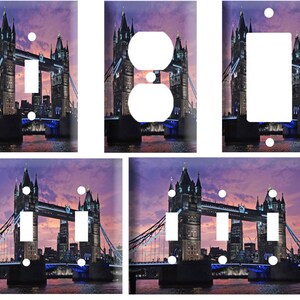 May include: A set of four light switch and outlet covers featuring a photograph of the Tower Bridge in London at dusk. The image is a vibrant purple and pink with the bridge lit up in blue and white lights.
