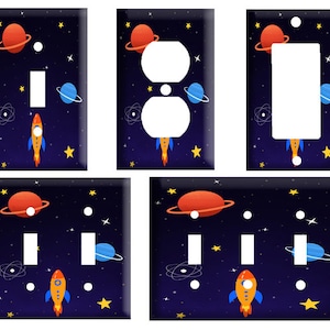May include: Set of six space-themed light switch covers. Each cover features a rocket ship, planets, and stars on a dark blue background. The covers are designed for standard light switches.
