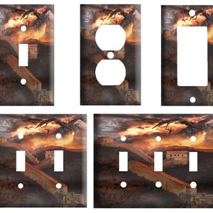 May include: Decorative light switch covers featuring a fantasy landscape with a dragon soaring over a fortress and a long wall. The color palette includes shades of orange, brown, and gray.