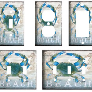 May include: Set of four light switch and outlet covers featuring a blue crab on a weathered wood background with the word "Beach" in white text.