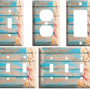 May include: Set of four light switch and outlet covers featuring a weathered blue and brown wood plank background with a white sandy beach and seashells.