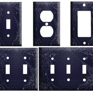 May include: Set of five Halloween-themed light switch and outlet covers featuring a dark blue brick background with white spiderwebs. The covers are available in single, double, and triple switch configurations.