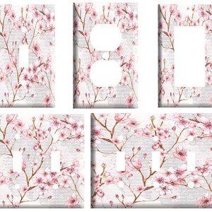 May include: Set of six light switch and outlet covers featuring a watercolor design of pink cherry blossoms on a white background.