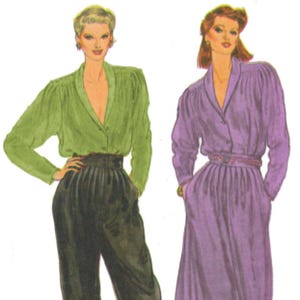 May include: A white ceramic mug with a black handle and the text "But First, Coffee" in a bold, black font. The mug is set against a blurred background, suggesting a cozy setting.