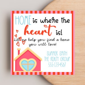 Puede incluir: Gráfico cuadrado rosa y blanco con el texto "HOME is where the heart is!" en una mezcla de fuentes. Una casa rosa con una ventana en forma de corazón está en la parte inferior. También se incluye el texto "Let me help you find a home you will love!"