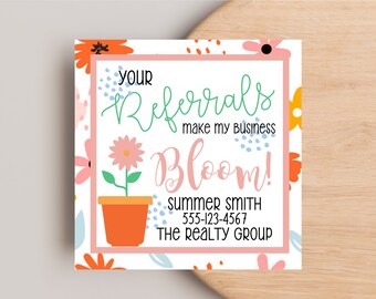 May include: A white business card with a floral design. The text reads "Your Referrals make my business Bloom!" followed by "Summer Smith" and a phone number. The card also includes the text "The Realty Group".