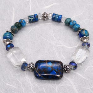 May include: A blue and green gemstone bracelet with silver accents and a large rectangular blue and brown gemstone in the centre.