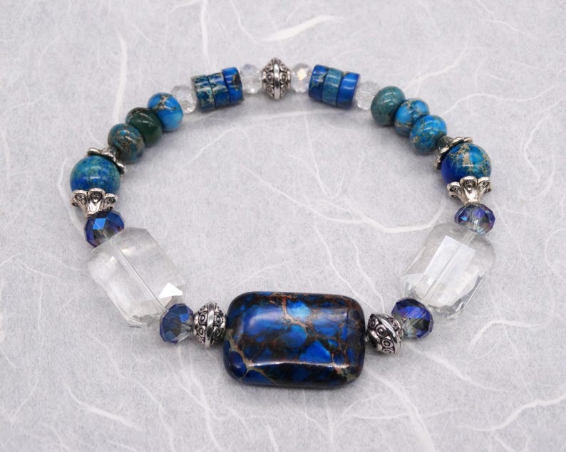 May include: A blue and green gemstone bracelet with silver accents and a large rectangular blue and brown gemstone in the centre.