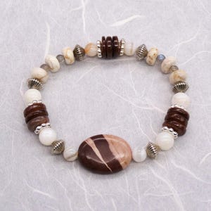 May include: A brown and white stone bracelet with silver accents. The bracelet features a large oval-shaped stone in the centre.