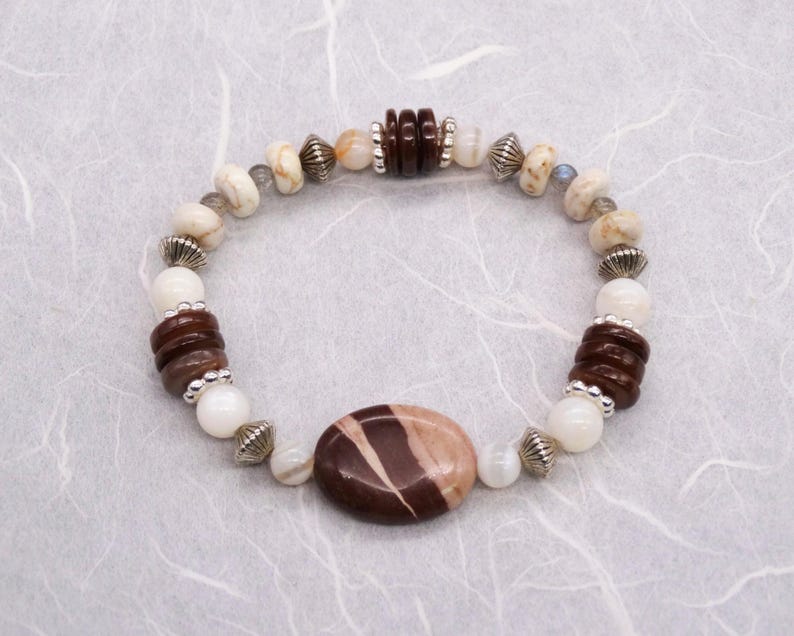 May include: A brown and white stone bracelet with silver accents. The bracelet features a large oval-shaped stone in the centre.