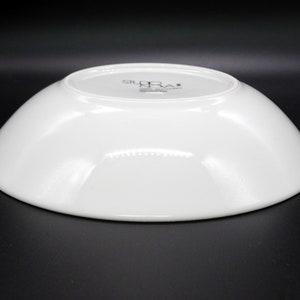 May include: White ceramic serving bowl with a slightly curved rim. The bottom of the bowl has the text "Studio Nova" printed in black.