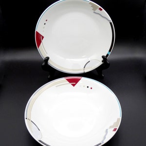 May include: Two white ceramic bowls with a geometric design in shades of red, blue, gray, and black. The bowls have a white interior and a rim with a blue and gray stripe.
