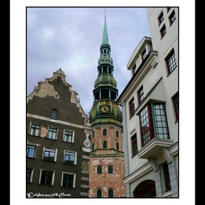 May include: A tall, green-roofed church with a clock tower stands in the middle of the image. The church is surrounded by older buildings with red tile roofs. The sky is cloudy and gray.