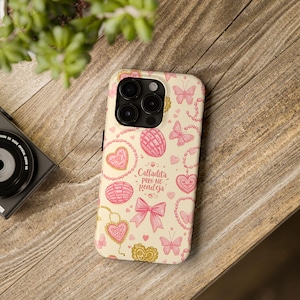 May include: A phone case with a cream background and a repeating pattern of pink butterflies, hearts, and concha pastries. The case also features the text "Calladita pero no pendeja" in pink.