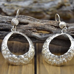 May include: Silver hoop earrings with a textured, hammered finish. The earrings have a circular shape with a small bead at the top.