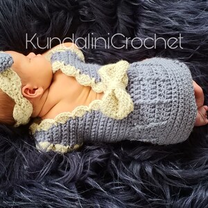 May include: A newborn baby wearing a crocheted outfit in shades of gray and yellow. The outfit features a bow and a headband. The baby is lying on a black fuzzy surface. The text "KundaliniCrochet" is visible in the image.