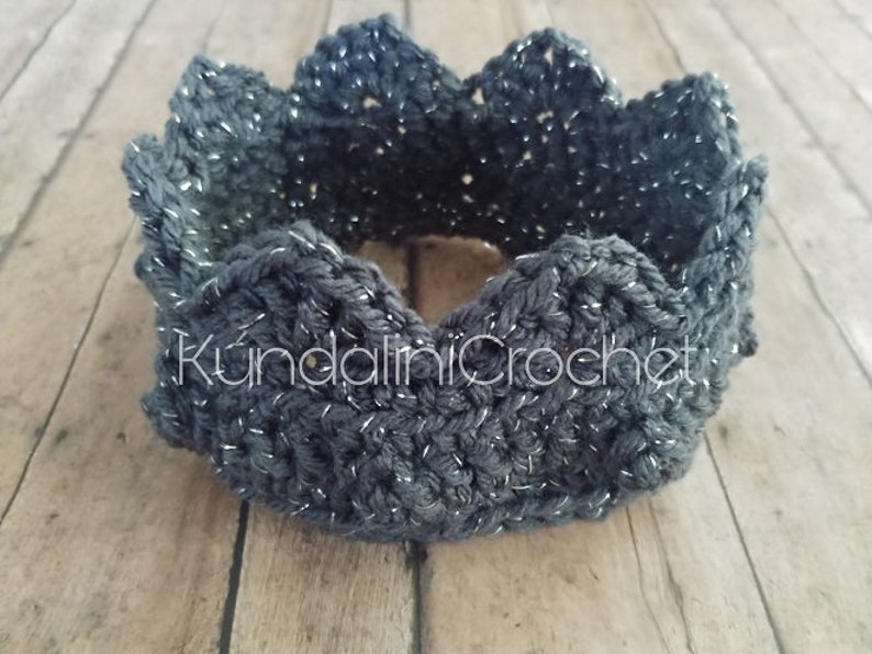 May include: A dark gray crocheted crown with silver glitter thread. The crown is made with a simple stitch pattern and has a scalloped edge.