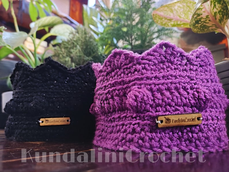 May include: Two crocheted plant pot covers, one black and one purple, with wooden tags that say "Kundalini Crochet" and "Lodie's Craft".