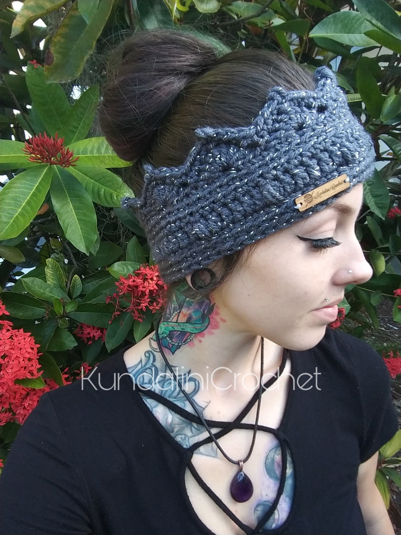 May include: A gray crocheted crown headband with silver glitter. The headband has a small wooden tag with the text "Kundalini Crochet" on it.