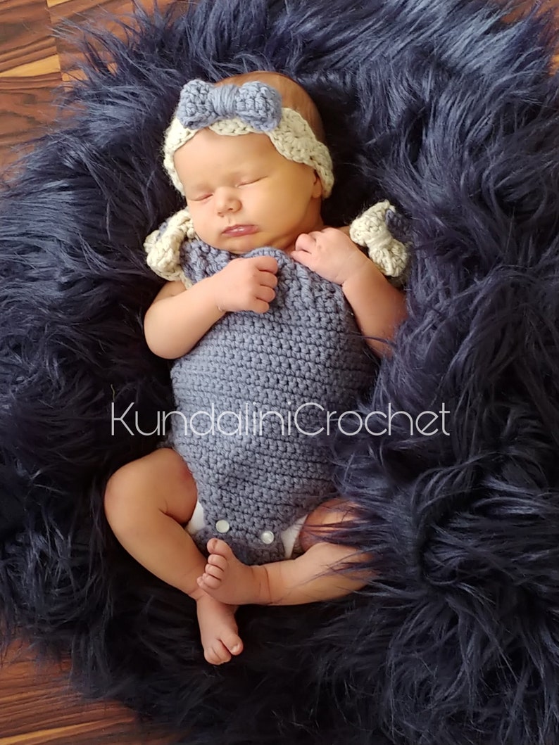 May include: A baby wearing a crocheted blue and white outfit with a white crocheted headband. The baby is lying on a blue fuzzy blanket.