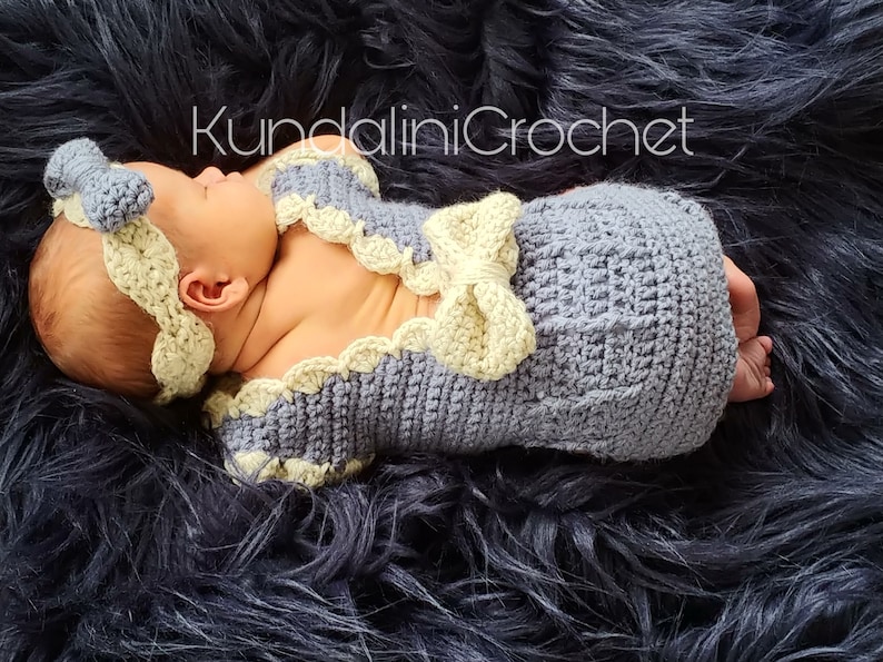 May include: A newborn baby wearing a crocheted outfit in shades of gray and yellow. The outfit features a bow and a headband. The baby is lying on a black fuzzy surface. The text "KundaliniCrochet" is visible in the image.
