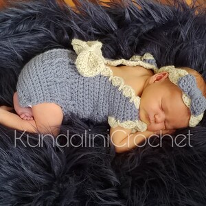 May include: A sleeping baby wearing a crocheted gray and white outfit with a matching headband. The baby is lying on a black fuzzy surface. The text "Kundalini Crochet" is visible in the image.