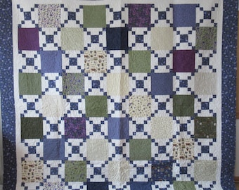 May include: A quilt with a blue, white, green, and purple patchwork design. The quilt is made up of squares of different fabrics, each with a different pattern. The quilt is edged with a blue border.
