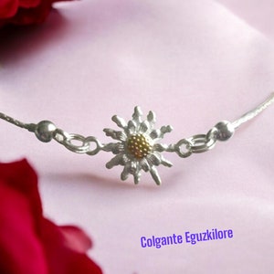 May include: A silver chain necklace with a delicate daisy charm. The daisy has a gold center and silver petals. The necklace is on a pink background with a red rose.