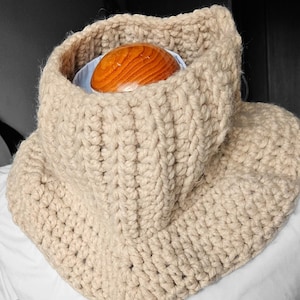 May include: A beige crocheted cowl neck warmer. The text "Cuello tejido" is visible at the bottom of the image.