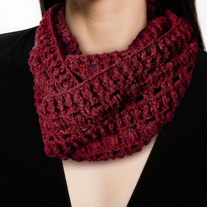 May include: A deep burgundy infinity scarf featuring an open, textured crochet pattern. The yarn is a rich, dark red color with a visible looped stitch construction that creates a lightweight, airy appearance around the neck area.