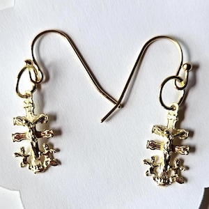 May include: A pair of gold-tone earrings with a detailed cross pendant featuring a figure of Jesus Christ. The cross has four arms and is adorned with smaller crosses at the ends of each arm.