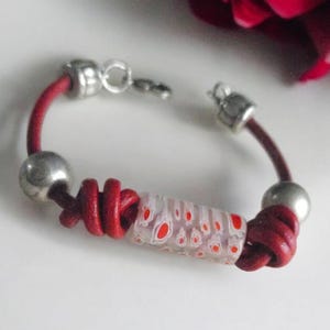 May include: A red leather bracelet with silver beads and a white and red glass bead. The bracelet is knotted and has a silver clasp.